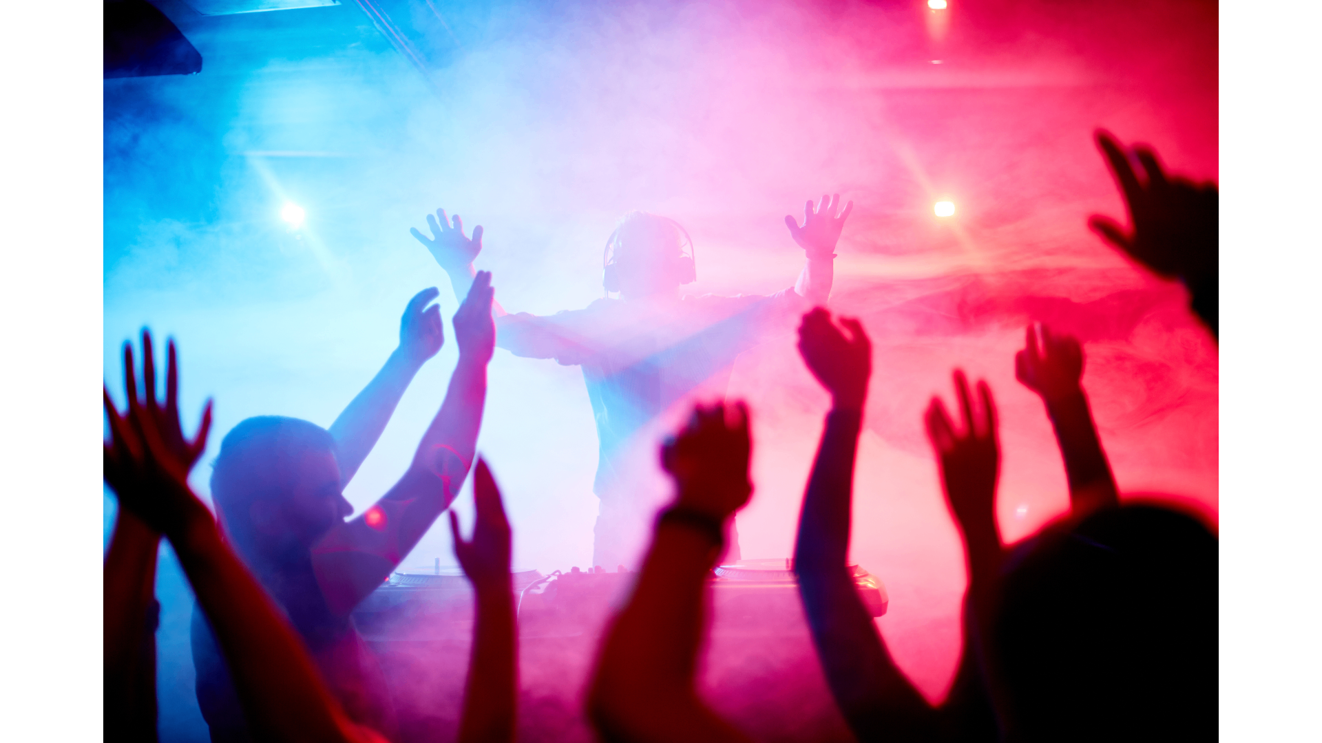 Crowd celebrating in front of a DJ under vibrant blue and pink lights